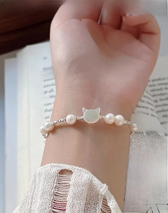 Macro detail of a s925 silver cat charm and freshwater pearl bracelet on a wrist