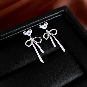 Detail of silver bow earrings featuring sparkling heart-shaped zircon on a black leather base