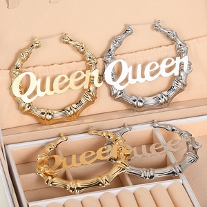 Makroaufnahme großer Gold- und Silber-Bambusohrringe mit dem Queen-Schriftzug für Damen