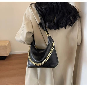 Close-up of black quilted leather hobo bag with a gold chain strap on a trench coat