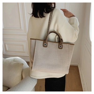 Beige canvas tote bag with brown leather trim and metal chain strap on shoulder