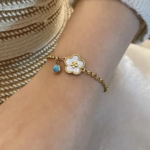Goldenes Gliederkettenarmband mit weißer Blume und blauem Charm am Handgelenk