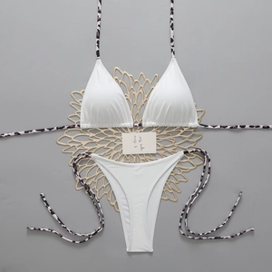 Flat lay of white triangle bikini set with leopard print ties on a decorative mat