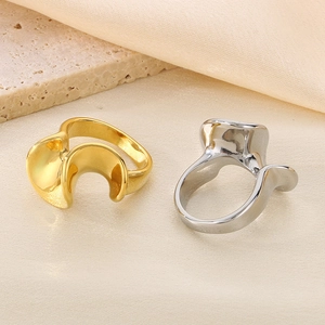 Close-up of gold and silver wavy stainless steel rings on a beige silk and travertine background