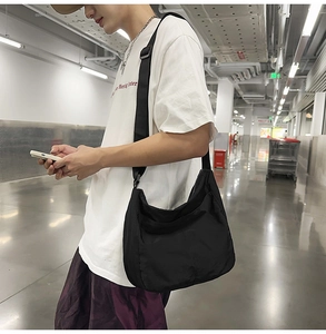 Detailed side view of large black nylon crossbody messenger bag worn by a model