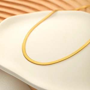 Minimalist golden snake bone chain necklace displayed on an elegant white tray