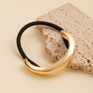 Macro view of gold C-shaped metal ornament on black elastic hair tie with stone texture