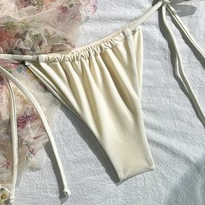 Detail view of cream tie-side bikini bottom with floral mesh ruffle and smooth texture