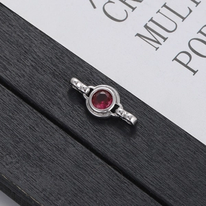 Minimalist silver bracelet charm with a round red zircon inlay on dark wood