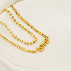 Detail of double-layer gold chain bracelet with beads and LOVE pendant on white texture