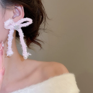 Close-up of pink plush bow earrings with pearl drops and snowflake accents on model