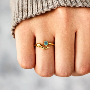 Detailed view of a gold snake ring with a blue gemstone on a finger for fashion
