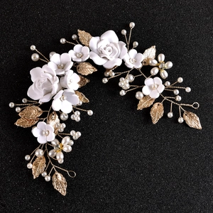 Detail of white ceramic flowers and golden metal leaves with pearls bridal hairpiece