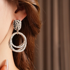 Close-up of geometric hammered silver earrings featuring multi-layered round hoops