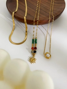 Detailed shot of layered 18K gold-plated beaded necklaces with sun and pearl pendants
