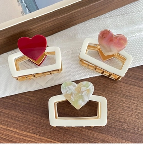 Detail of 6cm heart claw clips in red, amber pink, and green on wood surface