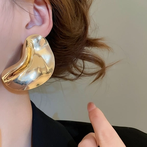 Close-up of model wearing irregular gold wave earrings with a high-shine mirror finish