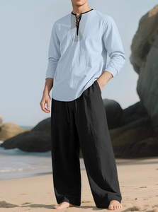 Detail of light blue linen shirt with frog buttons and black trousers on a beach
