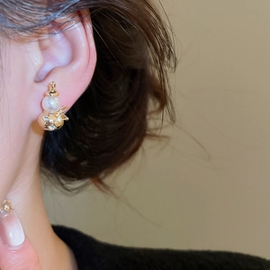 Close-up of elegant gold gourd earrings with white pearl and sparkling crystals on model
