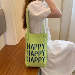 Close-up of light green canvas tote bag with Happy lettering worn by a model