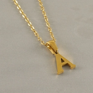 Macro shot of gold letter A pendant with fine chain on textured grey fabric