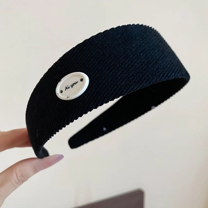 Détail de la texture en velours côtelé noir du serre-tête avec une plaque logo ovale blanche