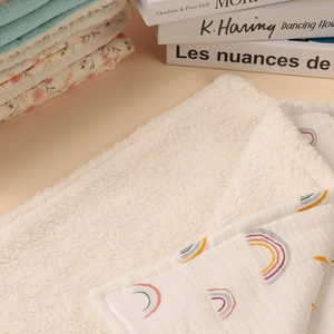 Detail of baby blanket showing cotton rainbow print and thick white sherpa fleece texture