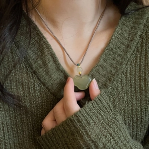 Detail of hand-woven rope necklace with cyan jade ruyi lock pendant on a green sweater