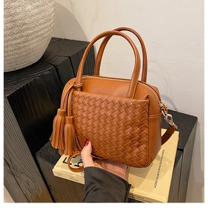 Close-up of brown woven leather handbag with fringe detail on rustic decorative books