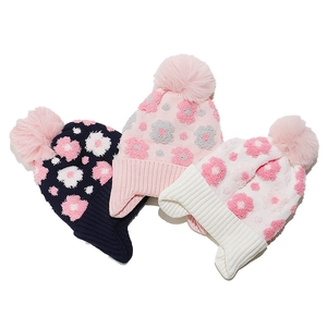Detailed flat lay of knit earflap beanies with floral patterns and plush pom-poms