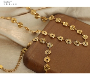 Detailed close-up of golden spiral link necklace on champagne silk and wood
