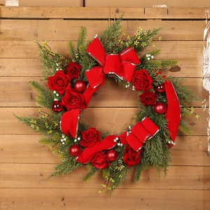 Christmas wreath with red roses, ribbons and pine needles on a rustic wooden background