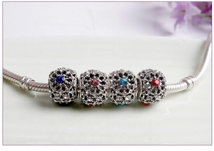 Macro shot of silver hollow charms set with blue, pink, and red gems on a snake chain
