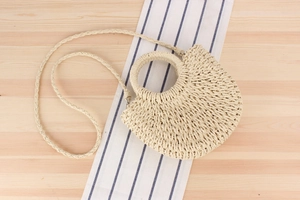 Detail of minimalist woven semi-circle straw bag with round handle and shoulder strap