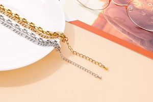 Detail of gold and silver layered necklace on a ceramic plate with Figaro chain style