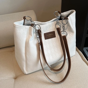 Large white quilted tote bag with brown straps and silver chain on a leather sofa