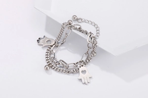 Macro detail of silver layered bracelet with Hamsa Hand and heart-shaped cutout pendant
