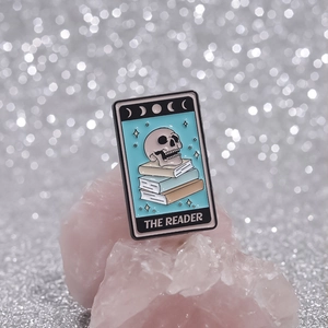 The Reader tarot style enamel pin featuring a skull reading books with moon phases