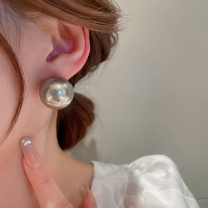 Gros plan d'une grande boucle d'oreille sphérique en argent poli sur un modèle