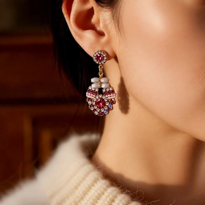 Close-up of vintage gold earrings with red stones and a white bow worn by a model