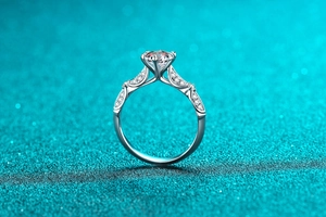 Detail of silver moissanite ring with six-prong setting and pavé diamonds on twisted band