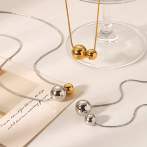 Collier chaîne serpent avec pendentifs boules dorées et argentées sur verre décoratif