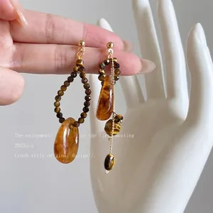 Asymmetric earrings with tiger eye stone and resin charms held by hand