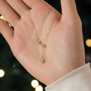 Detail of elegant gold necklace with zircon pendant held in hand on warm background