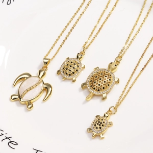 Set of four gold turtle necklaces with white shell and zircon pendants on a ceramic plate