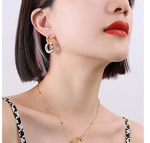 Detail of model wearing interlocking two-tone earrings and a fine gold chain necklace