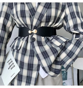 Close-up of black elastic waist belt with gold round buckle on checkered blazer