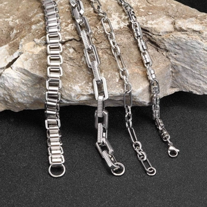 Macro detail of four men's stainless steel chain bracelets on natural rock surface