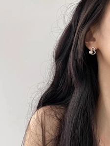 Close-up of sparkling zircon and pearl gourd earrings worn on ear with silver finish