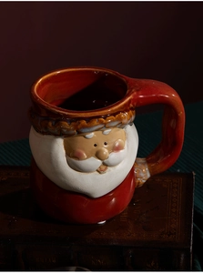 Detail of red ceramic Christmas mug with a 3D Santa Claus embossed design on dark vintage books